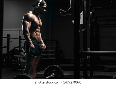 Muscular athletic bodybuilder man hard workout  in gym over dark background with dramatic light with barbell