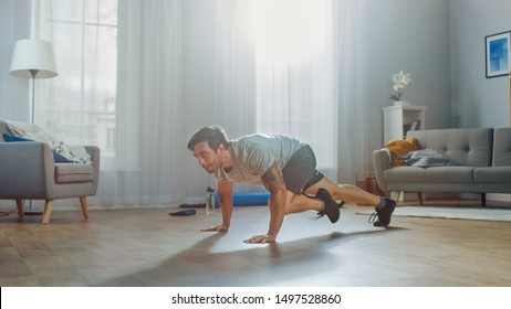 Muscular Athletic Fit Man In T-shirt And Shorts Energetically Starts Doing Mountain Climber Exercises At Home In His Spacious And Bright Apartment With Modern Interior.