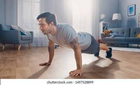 Muscular Athletic Fit Man In T-shirt And Shorts Is Doing Push Up Exercises At Home In His Spacious And Bright Apartment With Minimalistic Interior.