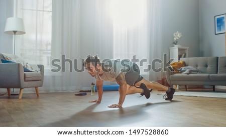 Muscular Athletic Fit Man in T-shirt and Shorts Energetically Starts Doing Mountain Climber Exercises at Home in His Spacious and Bright Apartment with Modern Interior.