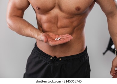 Muscular Athletic Guy With A Naked Torso Is Holding Vitamins And Steroids Pills. Sports And Supplements. Healthy Lifestyle And Medicine 