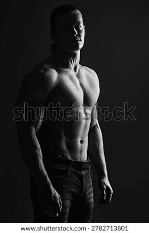 Muscular athletic man posing in dramatic low key lighting. Strong male body, fitness concept, bodybuilding, power and masculinity, isolated on dark background with copy space.