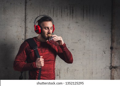 Muscular Athletic Man Wearing Sportswear And Carrying A Gym Bag, Listening To The Music And Eating A Protein Bar After A Hard Workout