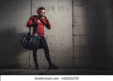 Muscular Athletic Man Wearing Sportswear And Carrying A Gym Bag, Listening To The Music And Eating A Protein Bar After A Hard Workout