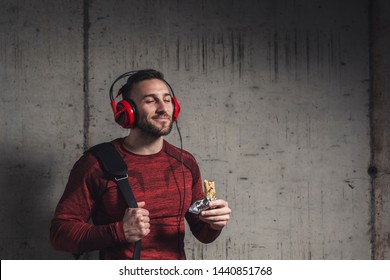 Muscular Athletic Man Wearing Sportswear And Carrying A Gym Bag, Listening To The Music And Eating A Protein Bar After A Hard Workout