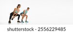 Muscular athletic young couple, man and woman doing squats exercises with kettle bell, training against white studio background. Concept of sport, active and healthy lifestyle, workout, fitness