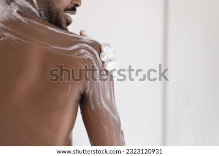 Muscular back of bearded guy, taking shower, applying foamy gel or soap on smooth dark skin. Male morning bath routine, daily hygiene, bodycare concept. Cropped shot, close up