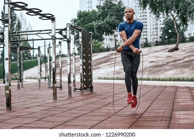 Muscular black man skipping rope. Portrait of muscular young man exercising with jumping rope on national park background - Powered by Shutterstock