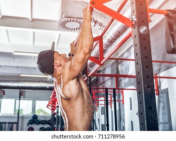 Muscular bodybuilder doing pull ups exercise on bar at gym