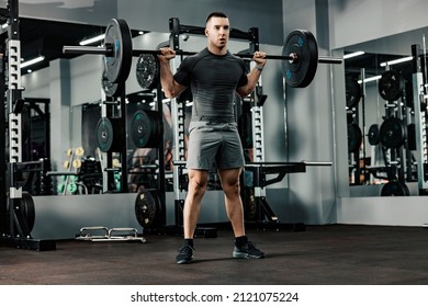 A muscular bodybuilder doing strength exercises with weights in a gym. - Powered by Shutterstock