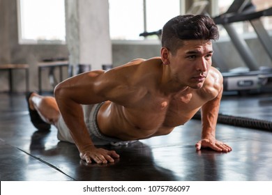 Muscular bodybuilder guy doing push ups exercise  in fitness gym . Shirtless young sport man training 