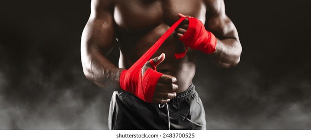 A muscular boxer prepares for a fight by wrapping his hands with red tape. - Powered by Shutterstock