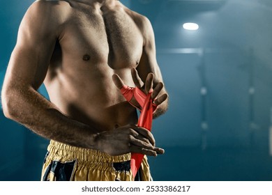 Muscular boxer is wrapping his hands with red boxing wraps in a gym, getting ready for an intense workout - Powered by Shutterstock