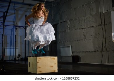 Muscular Bride In A Wedding Dress Doing Exercises On A Wooden Box In The Gym.