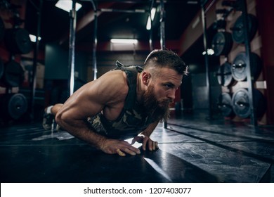 Muscular Caucasian Bearded Man Doing Push-ups In Military Style Weighted Vest In Gym. Weight Plates In Background.