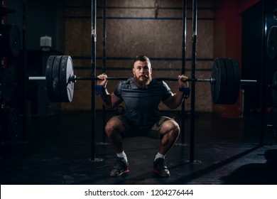 Muscular Caucasian Bearded Man Lifting Weights And Doing Back Squat In Gym.