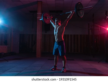 Muscular Caucasian man with muscular body doing barbell overhead press in a dark grungy gym with blue red neon light - Powered by Shutterstock