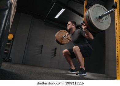 Muscular caucasian man lifting weights and doing back squat in gym. Crossfit athlete is holding a heavyweight barbell on the shoulder behind the neck while squatting. Fitness and work out - Shutterstock ID 1999113116