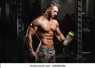 Muscular Caucasian Man On Diet Resting After Exercise And Drinking Protein Powder From Shaker In The Gym