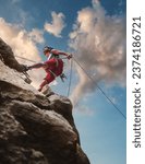 Muscular climber man in protective helmet abseiling from cliff rock wall using rope Belay device and climbing harness on evening sunset sky background. Active extreme sports time spending concept.