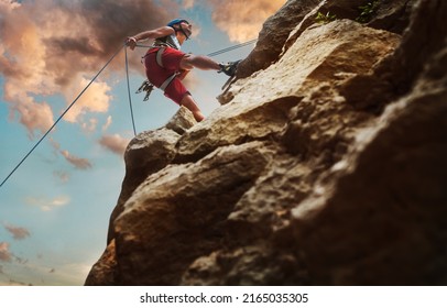 Muscular climber man in protective helmet abseiling from cliff rock wall using rope Belay device and climbing harness on evening sunset sky background. Active extreme sports time spending concept. - Shutterstock ID 2165035305