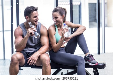 Muscular couple discussing on the bench and holding water bottle