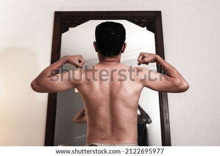 muscular entry level Asean young  man posing infront of a mirror.
