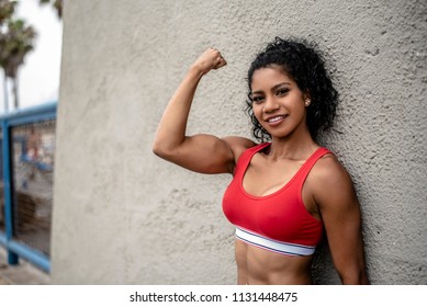 A Muscular Female Athlete Wearing A Red Sports Bra Flexes Her Arms Showing Her Muscle Tone