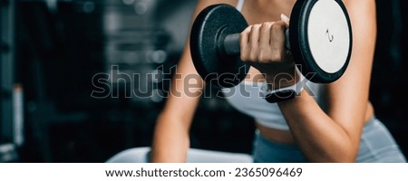 A muscular female lifting dumbbells on a bench at the gym to exercise her arm muscles and build up her strength and endurance for an active lifestyle, fitness GYM dark background