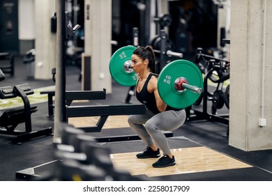 A muscular female weightlifter is doing exercises in a gym with barbell while squatting. - Powered by Shutterstock