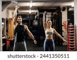 Muscular fit friends standing in a gym and lifting kettle bells.