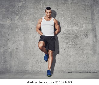 Muscular and fit man relaxing after workout, leaning against grey background, wearing white tank top and black shorts - Powered by Shutterstock