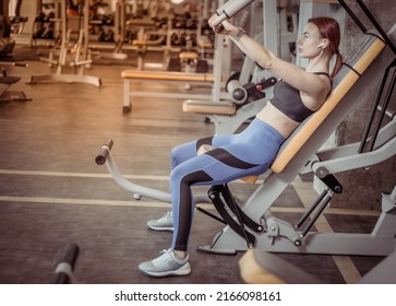 Muscular Fit Redhead Woman Trains Chest Muscles In Exercise Machine At The Gym