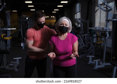 Muscular Fitness Coach And His Senior Client Wearing Medical Face Masks During Gym Workout