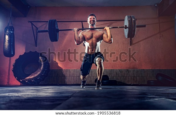 Muscular fitness\
man doing barbell lunges in his garage, selfisolation. Functional\
training. Snatch\
exercise.