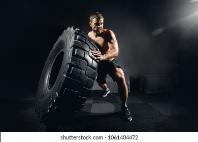 Muscular fitness shirtless man moving large tire in gym center, concept lifting, workout cross fit training