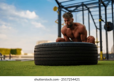 Muscular fitness trainer lifting a large tire during an outdoor workout on a sunny day. - Powered by Shutterstock