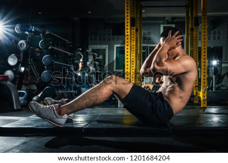 Muscular guy doing sit ups at gym with other people in background. Young athlete doing stomach workout in modern gym. Handsome fit man doing crunches at gym.