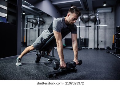 A muscular guy lifts a dumbbell while lying on a gym bench. A young athlete uses dumbbells during training. A strong man under physical exertion relaxes and stretches the muscles of the arms - Shutterstock ID 2109323372
