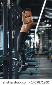 Muscular Guy With Naked Torso Pulling Up On Horizontal Bar In Gym, Empty Space