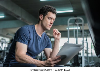 Muscular Handsome Trainer Looking At Fitness Plan On Clipboard For Working Out In The Fitness Gym.