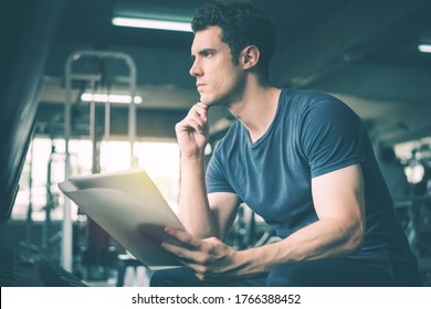 Muscular Handsome Trainer Looking At Fitness Plan On Clipboard For Working Out In The Fitness Gym