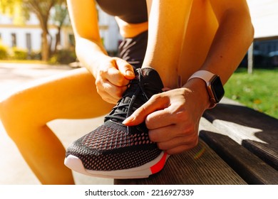 Piernas musculares de las chicas en las zapatillas deportivas para correr, pantalones cortos deportivos, con un reloj electrónico para el control de calidad de la formación. Las manos del atleta con un podómetro atan cordones de zapatos a las zapatillas deportivas. 