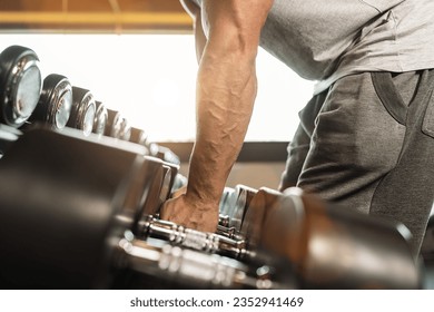 muscular male arm picking up heavy dumbbell weights from equipment rack in modern gym