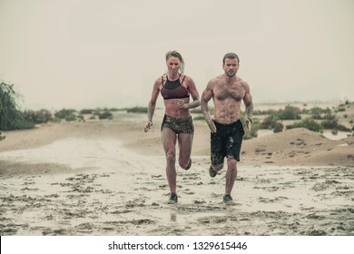 Muscular Male And Female Athlete Covered In Mud Running Down A Rough Terrain With A Desert Background In An Extreme Sport Race With Grungy Textured Finish