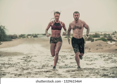 Muscular Male And Female Athlete Covered In Mud Running Down A Rough Terrain With A Desert Background In An Extreme Sport Race With Grungy Textured Finish