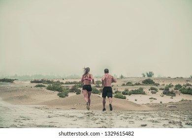 Muscular Male And Female Athlete Covered In Mud Running Down A Rough Terrain With A Desert Background In An Extreme Sport Race With Grungy Textured Finish