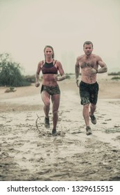 Muscular Male And Female Athlete Covered In Mud Running Down A Rough Terrain With A Desert Background In An Extreme Sport Race With Grungy Textured Finish