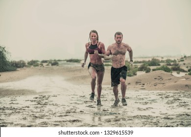 Muscular Male And Female Athlete Covered In Mud Running Down A Rough Terrain With A Desert Background In An Extreme Sport Race With Grungy Textured Finish