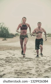 Muscular Male And Female Athlete Covered In Mud Running Down A Rough Terrain With A Desert Background In An Extreme Sport Race With Grungy Textured Finish